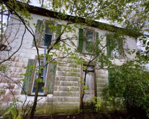 front of abandoned farmhouse with green shutters