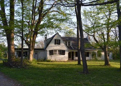 front of abandoned white brick farmhouse with crooked shutters