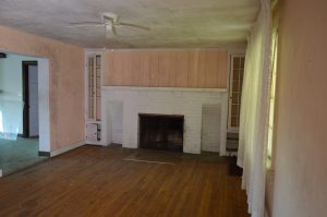 rool with ceiling fan and white brick fireplace in an abandoned house